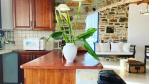 A kitchen with wooden cabinets, a white microwave, a potted plant, and a stone wall. - NikoRamaVilla  Swimming pool and BBQ with sea and mountains view (PAROS)