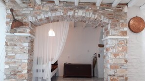 A stone-walled room with a bed, a hanging lamp, and a rustic wall decor. - NikoRamaVilla  Swimming pool and BBQ with sea and mountains view (PAROS)