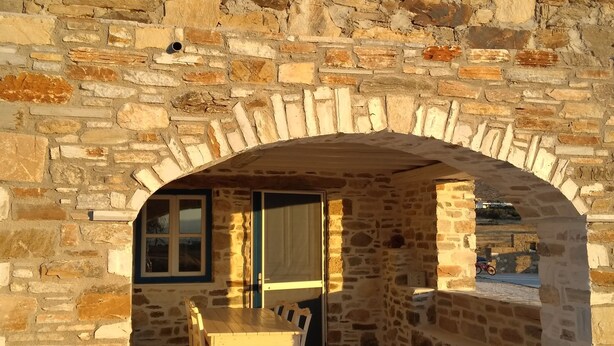 A stone archway leading to a patio area with a table and chairs. - NikoRamaVilla  Swimming pool and BBQ with sea and mountains view (PAROS)