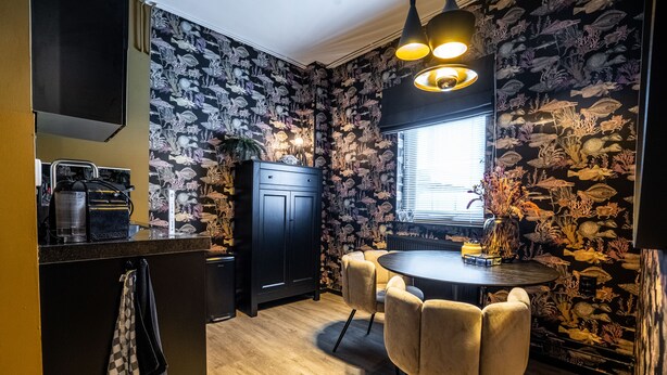 A kitchen with a black countertop, a black cabinet, a round table with chairs, and a wall with a fish pattern. - The Aquarium (Groningen)