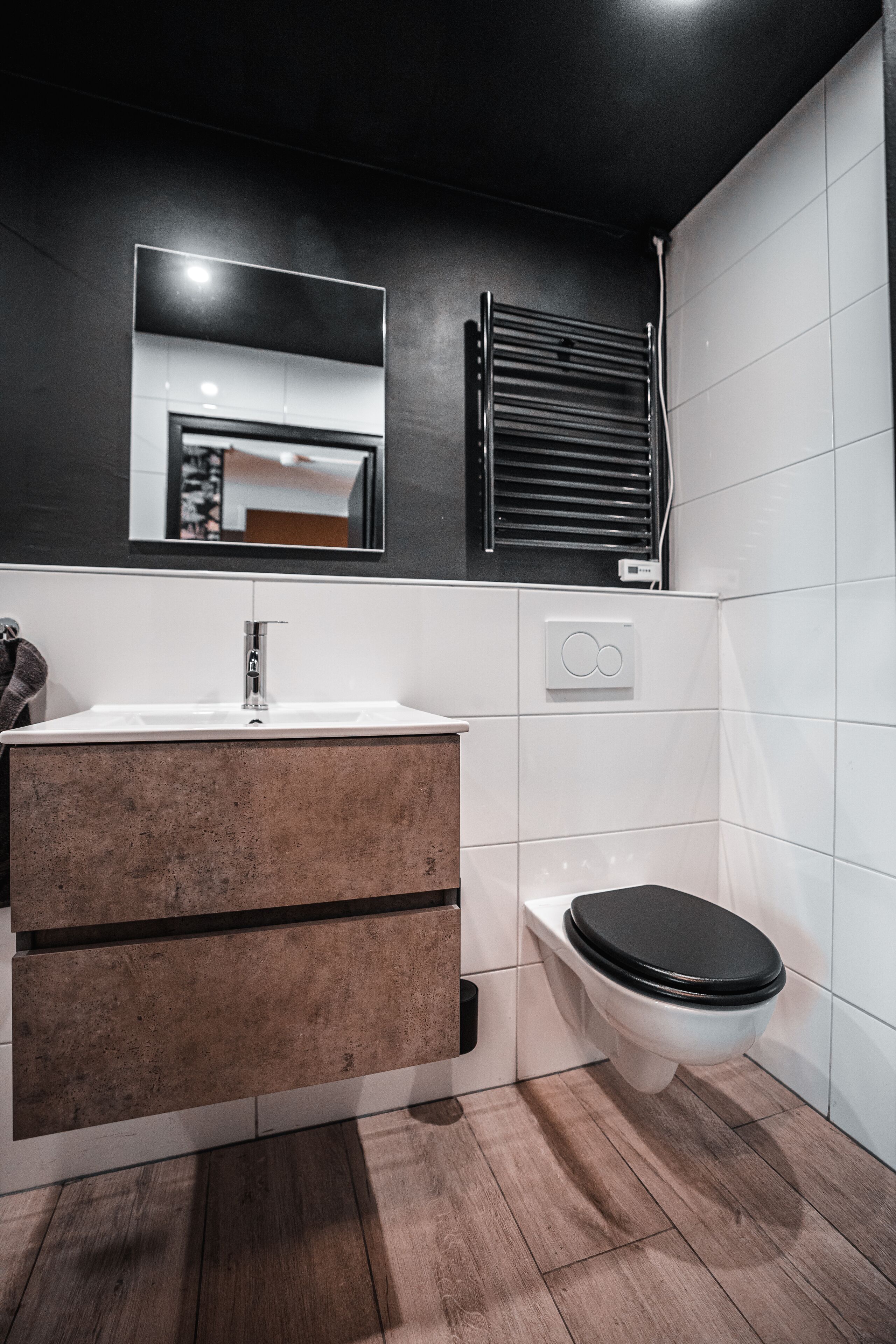 Et moderne badeværelse med en hvid vask, trækommode og et sort toilet.