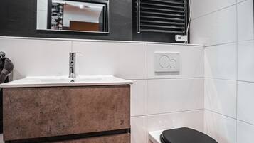 Et moderne badeværelse med en hvid vask, trækommode og et sort toilet.