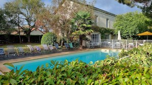 Une piscine avec des chaises longues, un patio clos et un bâtiment à la façade blanche.