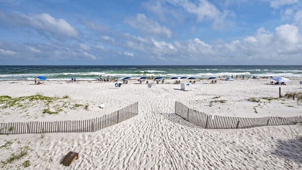 Une plage de sable avec une clôture en bois au premier plan, qui mène à l’océan.