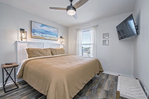 A bedroom with a bed, a ceiling fan, a mounted TV, and a window with blinds.