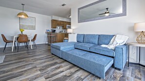 Un salon moderne avec un canapé d’angle, un coin repas avec une table et des chaises, et une cuisine en arrière-plan.