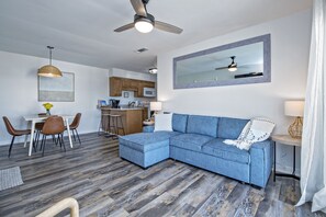 A modern living room with a sectional sofa, dining area, kitchen, and a ceiling fan.