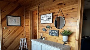 Ein Interieur einer Holzhütte mit Holzwänden, einem weißen Schrank, einem Willkommensschild, einer gerahmten Karte und einem Spiegel.