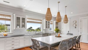 Uma cozinha moderna com armários brancos, uma ilha grande com banquetas e luminárias pendentes de vime.