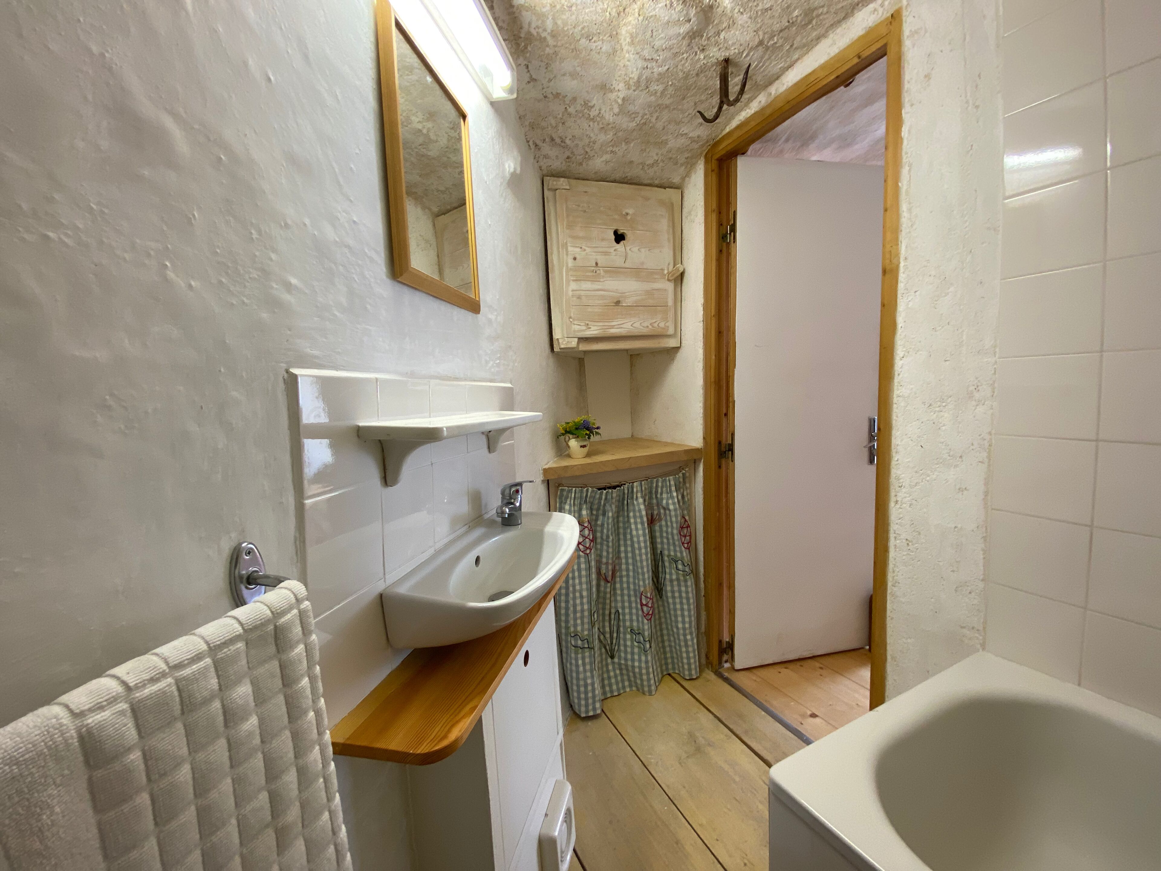 A bathroom with a sink, mirror, wooden shelf, and a bathtub.