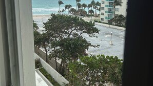 A view from a window overlooking a beach with palm trees and a tall building in the background.