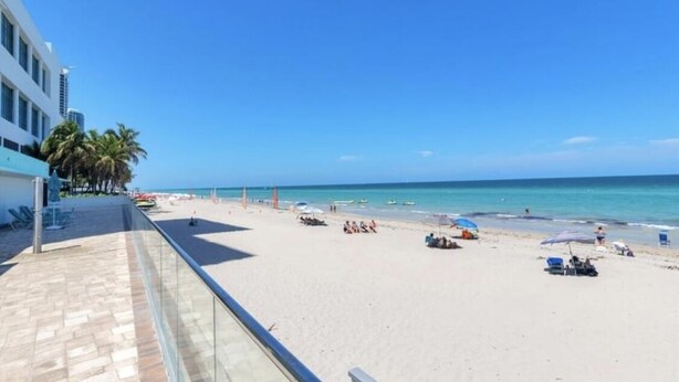 A beach with a clear sky, palm trees, and a building with a balcony overlooking the beach.
