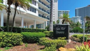 A modern hotel with a sign reading "Sea Air Towers" surrounded by well-maintained landscaping and palm trees.