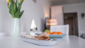 Une table à manger avec une assiette de nourriture, un vase de fleurs jaunes et un saladier de fruits en arrière-plan.