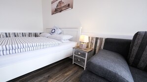 Une chambre à coucher bien rangée, avec un lit, une table de chevet dotée d’une lampe, un canapé gris et un tableau accroché au mur.