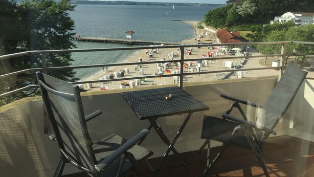 Un balcon offrant une vue sur une plage, une jetée et une côte lointaine.