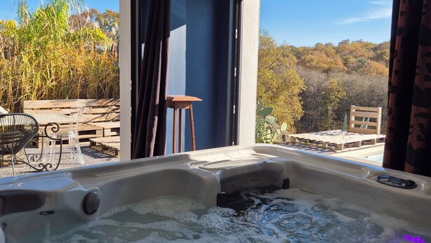 Un bain à remous dans une pièce dotée de grandes fenêtres, avec vue sur les arbres, et une terrasse en bois à l’extérieur.