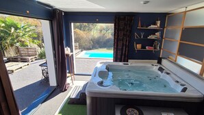Une chambre moderne dotée d’un jacuzzi, offrant une vue sur une piscine et comprenant un balcon aménagé avec du mobilier d’extérieur.