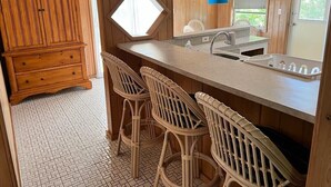 Eine Küche mit einem Holzkorpus, einer Bar mit Barhocker und einem großen Fenster.