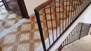 Una scala con ringhiera in legno e balaustre nere, che conduce a un pianerottolo con piastrelle decorate.