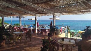 Zona salotto all'aperto con tavoli e sedie, con vista sul mare.