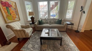 A living room with a sofa, armchair, coffee table, and a painting on the wall.