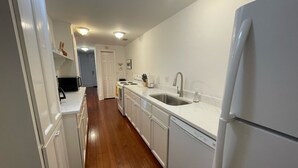 A narrow kitchen with white cabinets, a stainless steel sink, and a white refrigerator.
