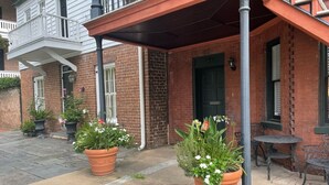 A brick building with a covered patio area, potted plants, and outdoor seating.