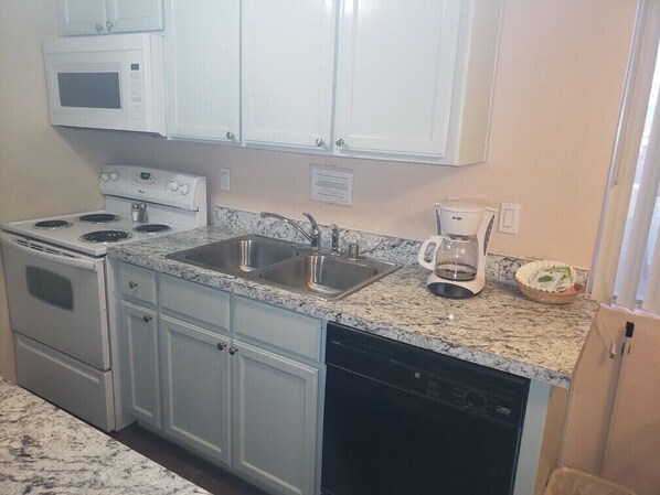 A kitchen with white cabinets, a granite countertop, a stove, a dishwasher, a sink, and a coffee maker.