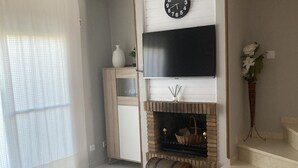 Olohuone, jossa on takka, seinälle asennettu televisio ja portaikko.