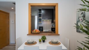A modern kitchen with a built-in window, white dining table with two chairs, and a small potted plant.