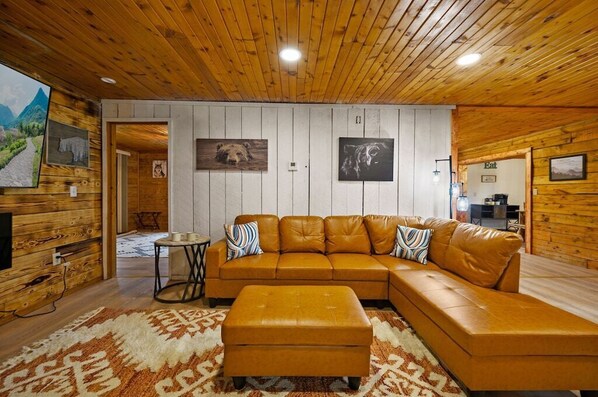 A cozy living room with a wooden ceiling, a large brown leather sofa, a matching ottoman, and a patterned rug. - "Outdoor private pool! game room, large deck" (Sevierville)