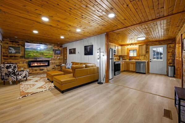 A cabin interior with a living room, kitchen, and fireplace.