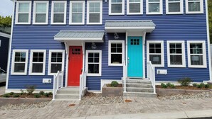 A two-story building with a red and a turquoise front door, white trim, and a small porch area. - Downtown Charlevoix, Riverwalk 107 (Charlevoix)