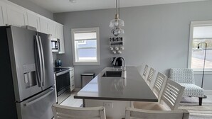 A modern kitchen with a central island, stainless steel appliances, and a hanging light fixture. - Downtown Charlevoix, Riverwalk 107 (Charlevoix)
