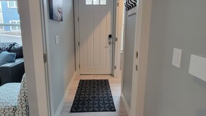 A hallway with a white door, a small window, and a black doormat. - Downtown Charlevoix, Riverwalk 107 (Charlevoix)