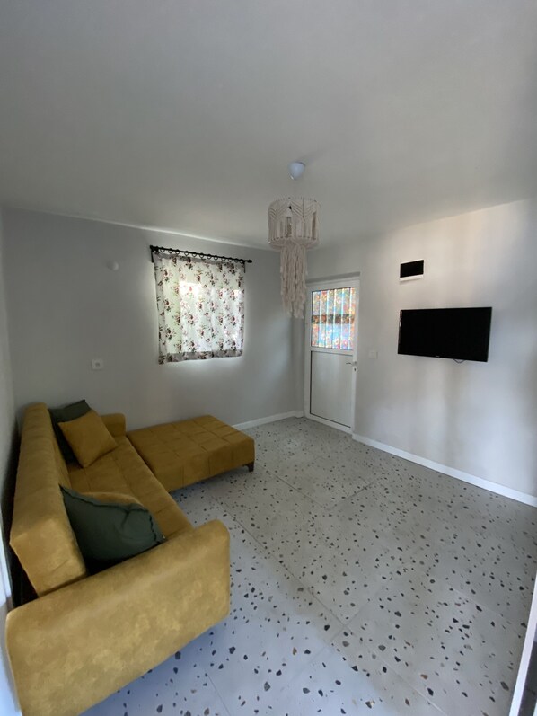 A living room with a sofa, a television mounted on the wall, and a window with curtains. - Seyyah Bozburun House (Marmaris)