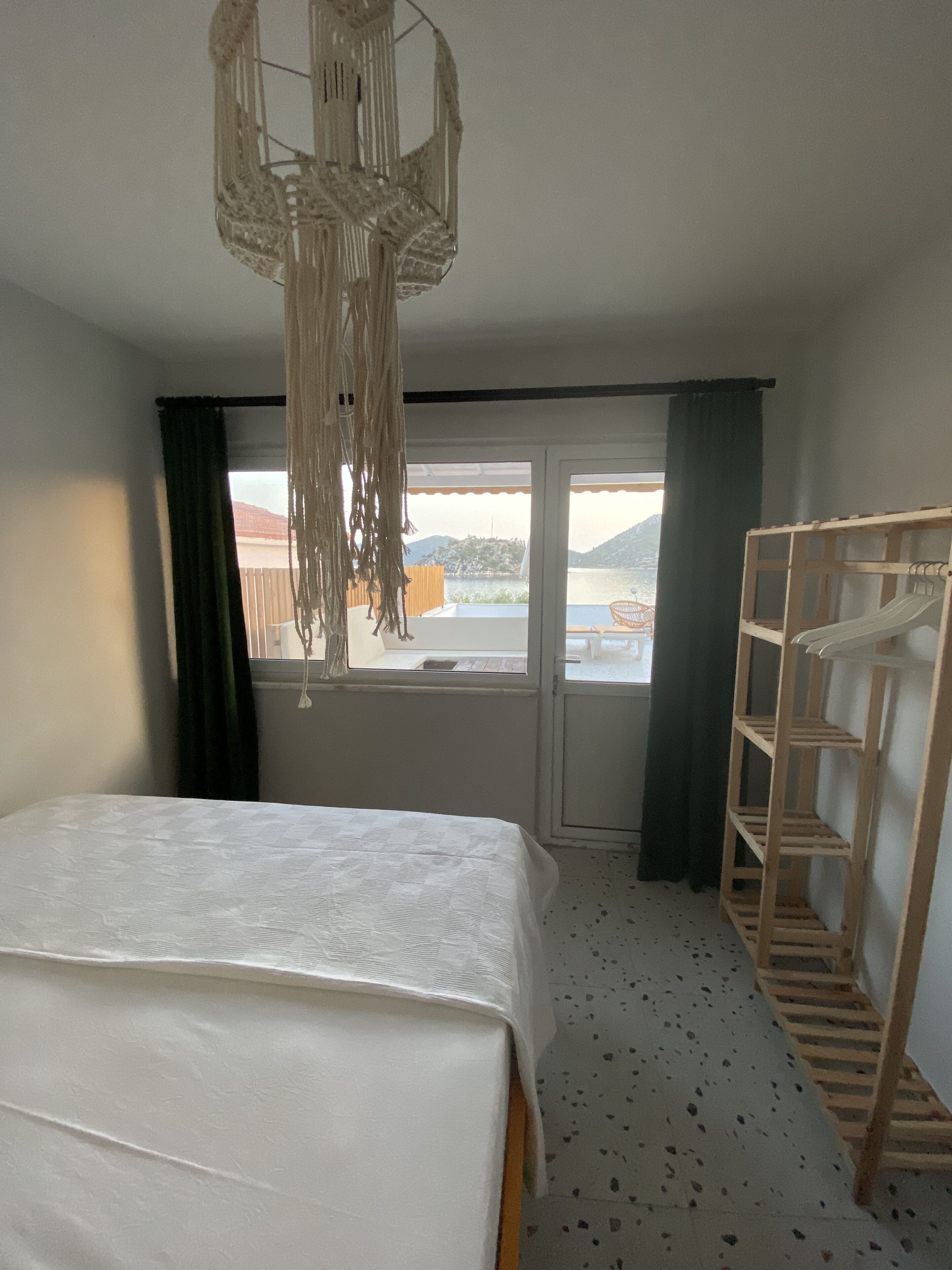 Una camera da letto con un letto, un mobile contenitore in legno, una lampada a sospensione e una finestra vista acqua e colline.