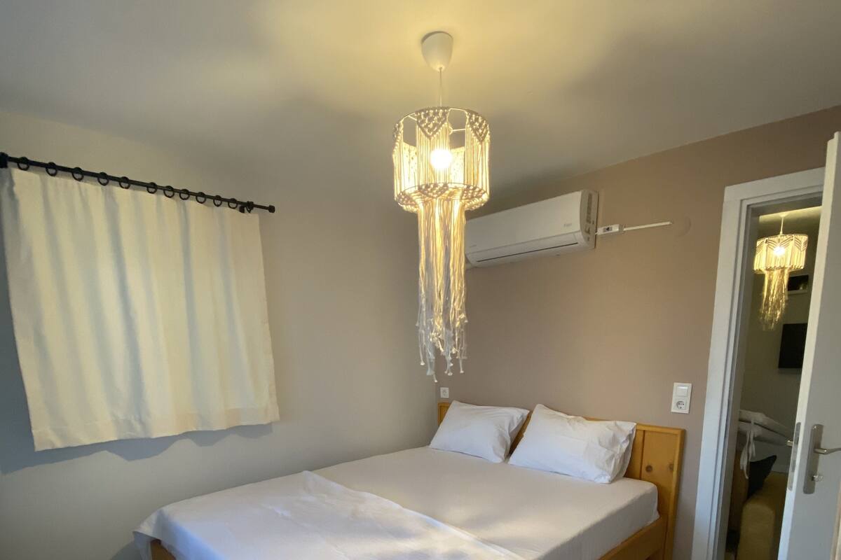 Une chambre à coucher comprenant un lit, un luminaire suspendu, un appareil de climatisation et une porte donnant sur une autre pièce.