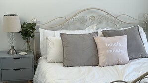 Un lit bien fait, avec une tête de lit en métal, une table de chevet avec une lampe et une petite plante.