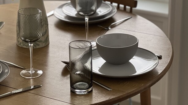Une table à manger ornée d’un vase de fleurs jaunes, d’un verre, d’un bol et d’une tasse.