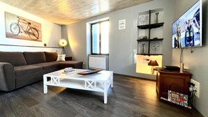 Een moderne woonkamer met een houten plafond, een bank, een witte salontafel, een televisie en een raam.