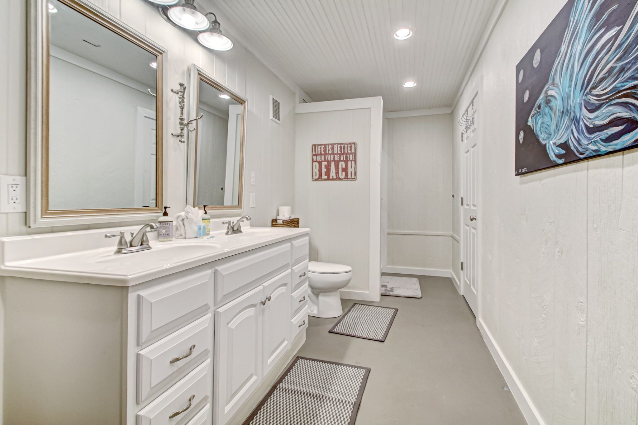 A bathroom with a white vanity, a large mirror, a toilet, and a wall-mounted artwork.