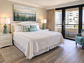 A hotel room with a large bed, two bedside tables, a window with curtains, a balcony, and a city view.