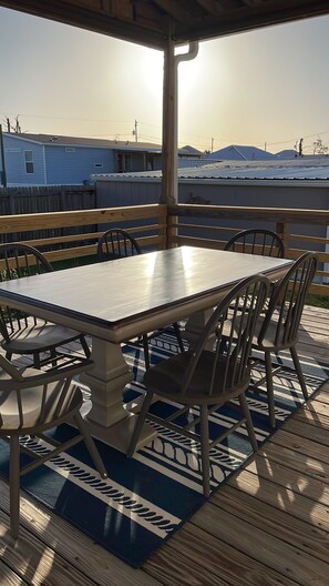 Un patio al aire libre con una mesa y sillas de madera, un tapete estampado y vistas a casas en el fondo.