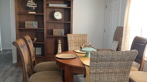 A dining area with a wooden table, four wicker chairs, a ceiling fan, and a bookshelf with various decorative items. - 5 minute walk to beach - come relax, enjoy family time and even fish. (Port St. Joe)