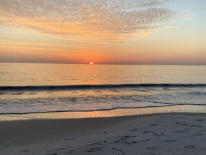 Una playa con huellas en la arena y un atardecer sobre el océano.