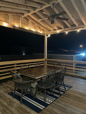 An outdoor wooden deck with a table and chairs, string lights, and a ceiling fan.