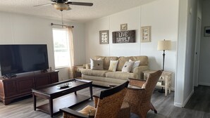 A living room with a sofa, two wicker chairs, a coffee table, a TV, and a ceiling fan. - 5 minute walk to beach - come relax, enjoy family time and even fish. (Port St. Joe)