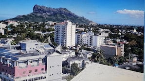 Un paisaje urbano costero con una montaña destacada al fondo, rodeado de edificios residenciales y un cielo azul despejado.